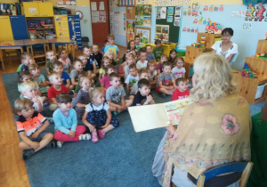 Aktorka czyta dzieciom opowiadania – dzieci siedzą na dywanie.